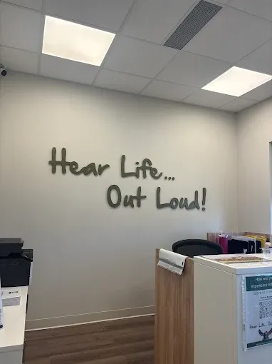 Inside a Calgary Hearing Aid & Audiology clinic, with 'Hear Life... Out Loud!' lettering on the wall
