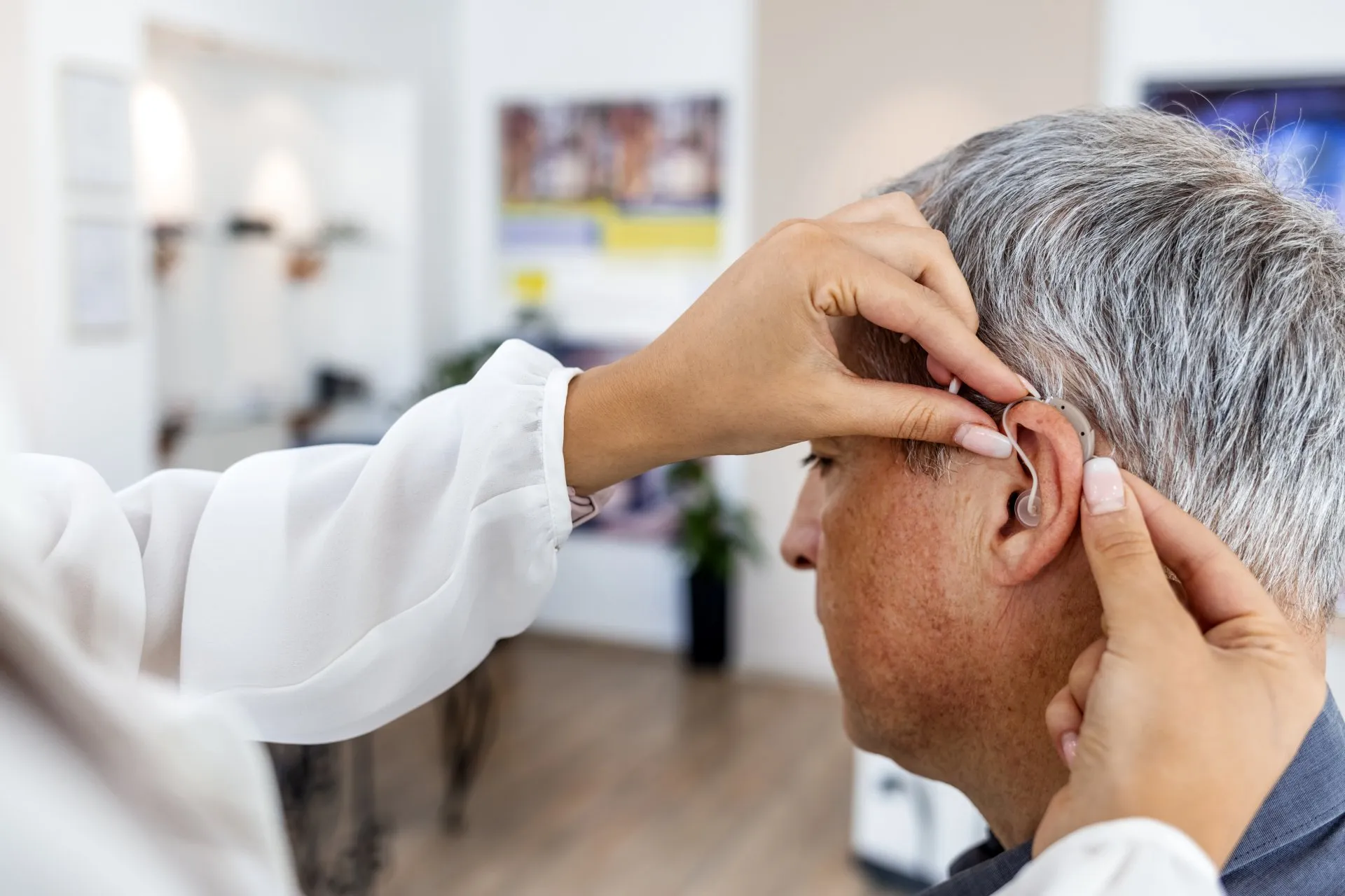 A hearing care professional fitting a behind-the-ear hearing aid on a client in the clinic